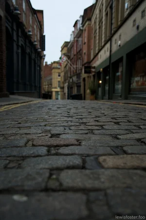 A quiet street scene in Sunderland at dusk, with wet pavement reflecting the lights from buildings and street lamps under a cloudy sky.